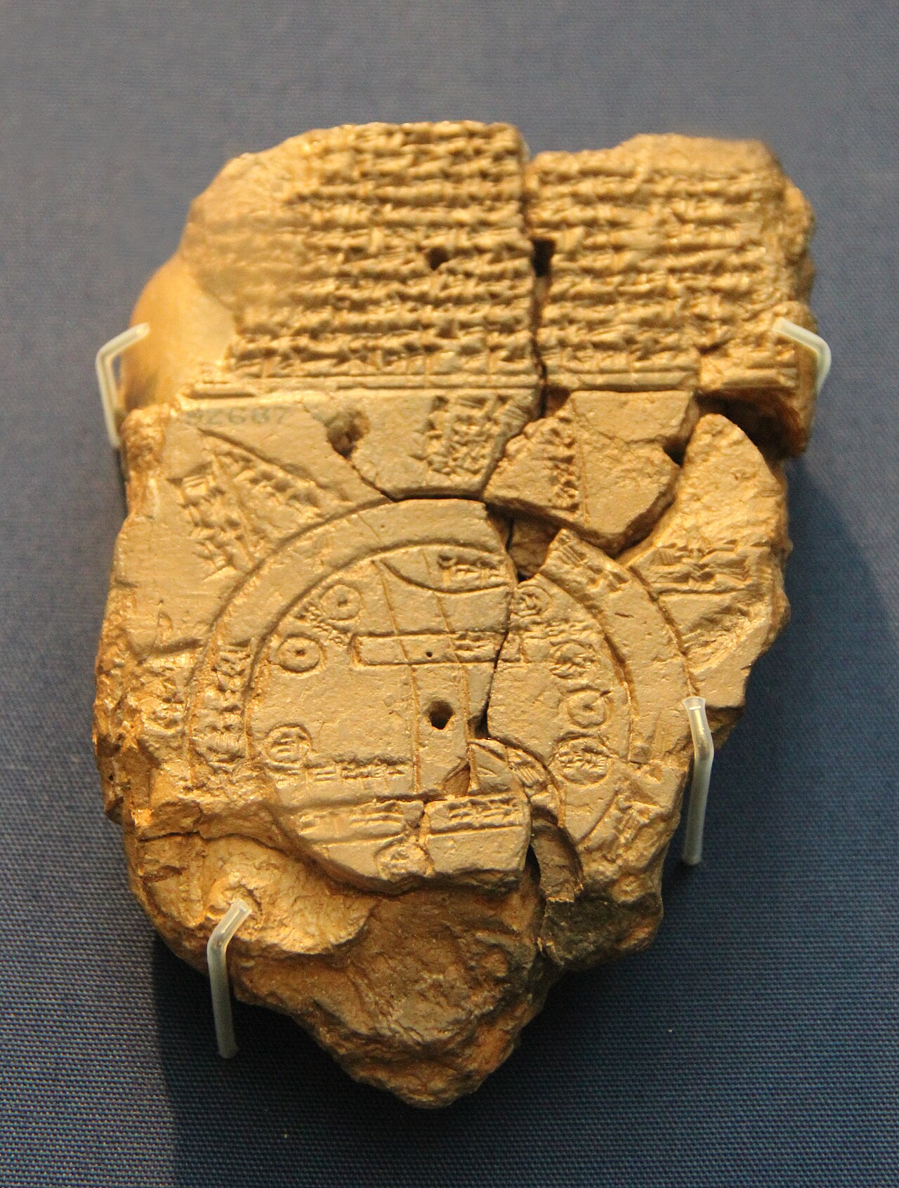 Clay tablet with cuneiform writing above a circular diagram and irregular broken edges.